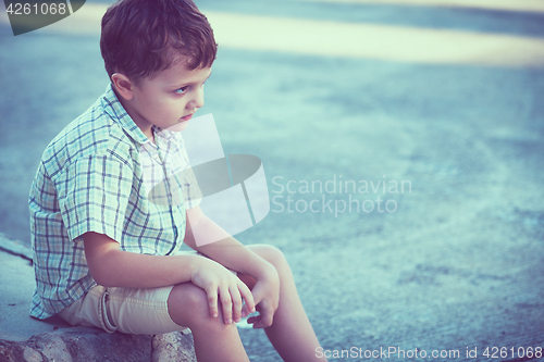 Image of Portrait of sad little boy sitting on street