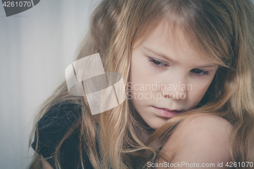 Image of Portrait of sad little girl sitting near the window
