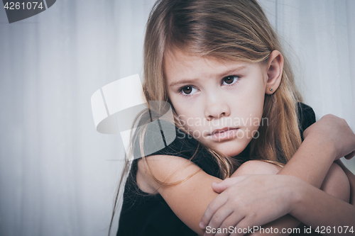 Image of Portrait of sad little girl sitting near the window