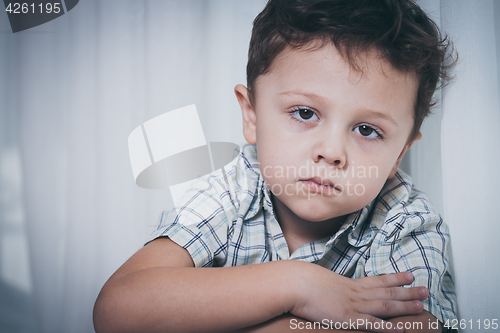 Image of Portrait of sad little boy sitting near the window