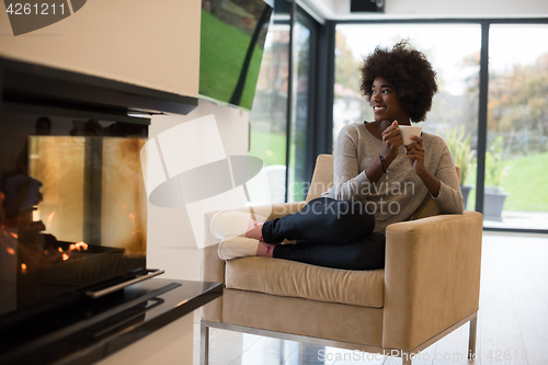 Image of black woman drinking coffee in front of fireplace