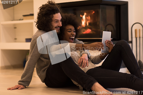 Image of multiethnic couple using tablet computer on the floor