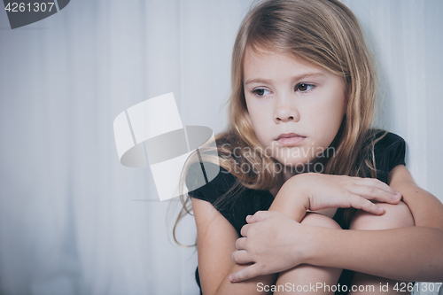 Image of Portrait of sad little girl sitting near the window