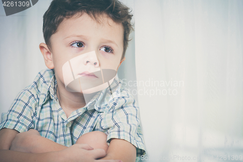 Image of Portrait of sad little boy sitting near the window