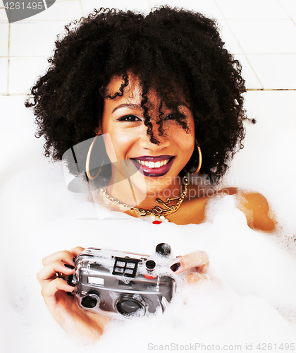 Image of young afro-american teen girl laying in bath with foam, wearing 