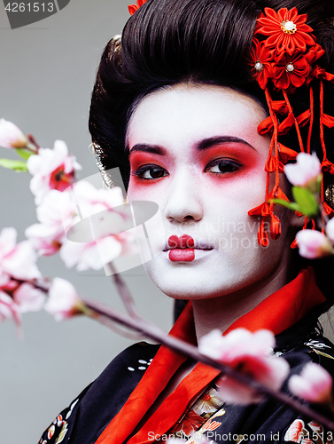 Image of young pretty geisha in black kimono among sakura, asian ethno close up