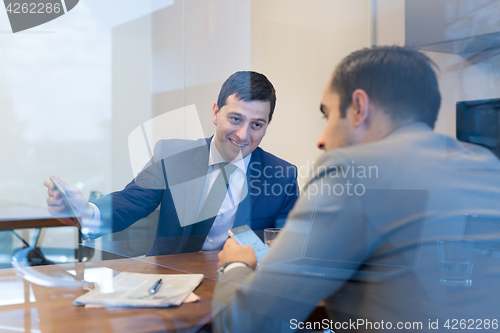Image of Two young businessmen using smart phones and touchpad at meeting.