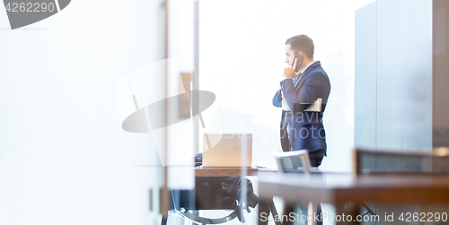 Image of Businessman talking on a mobile phone while looking through window.