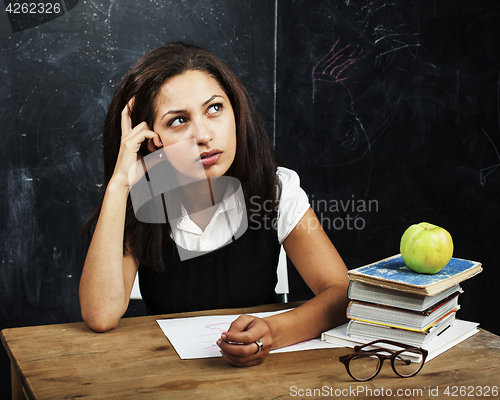 Image of young cute teenage girl in classroom at blackboard seating on ta