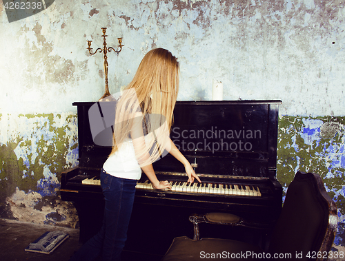 Image of pretty young blond real girl at piano in old-style rusted interi