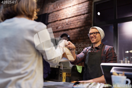 Image of woman taking paper bag from seller at cafe