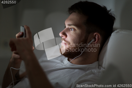 Image of man with smartphone and earphones in bed at night