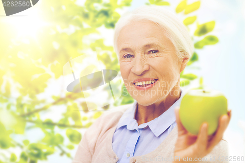 Image of happy senior woman with green apple at home