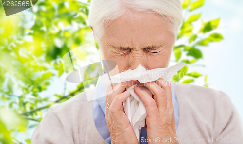 Image of sick senior woman blowing nose to paper napkin