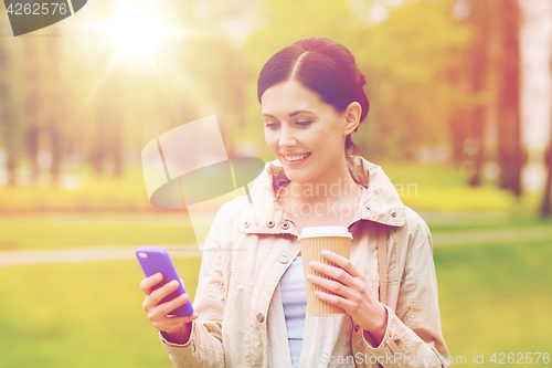 Image of smiling woman with smartphone and coffee in park