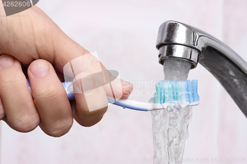 Image of hand washing toothbrush under running water