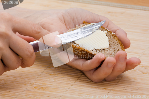 Image of woman hands spreading butter on piece of rye bread