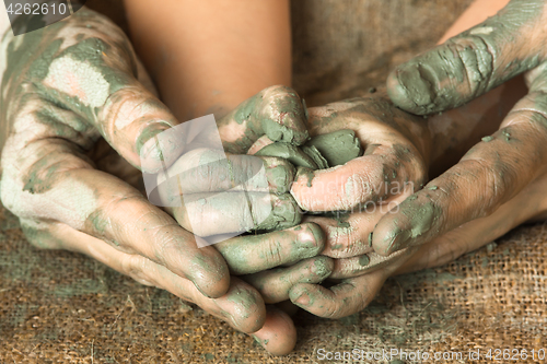 Image of hands of adult helping child to work with raw clay