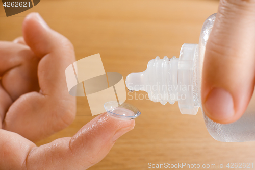Image of hands washing contact lens with solution