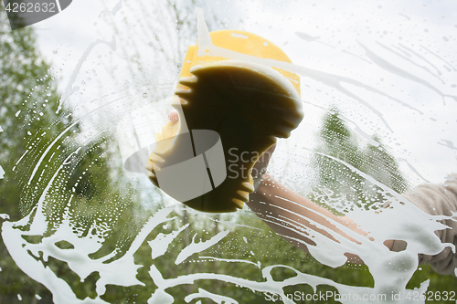 Image of hand with sponge washing the windscreen of a car, inside view