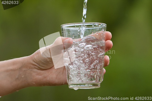 Image of hand pouring clean natural water into a glass, closeup