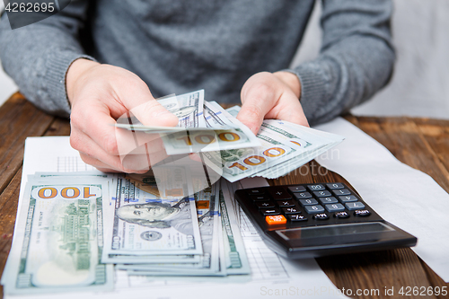 Image of Caucasian hands counting dollar banknotes on dark wooden table