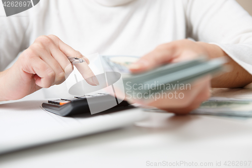 Image of savings, finances, economy and home concept - close up of hands with calculator counting money and making notes at home