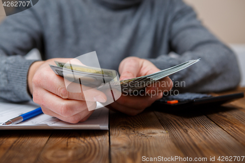 Image of Caucasian hands counting dollar banknotes on dark wooden table