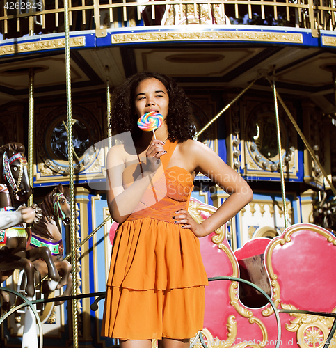 Image of cool real teenage girl with candy near carousels at amusement pa
