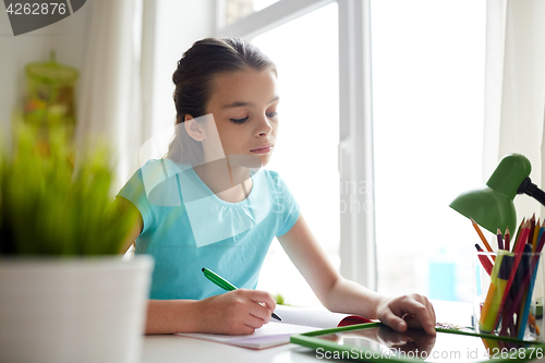 Image of girl with tablet pc writing to notebook at home
