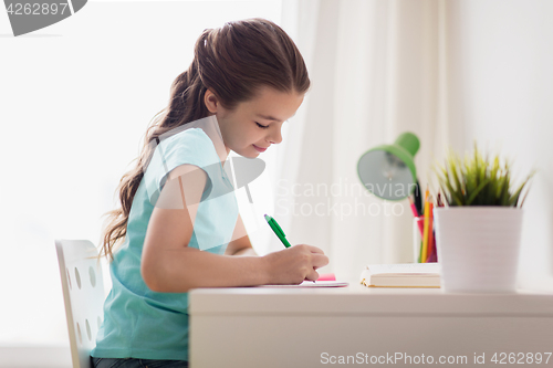 Image of happy girl with book writing to notebook at home