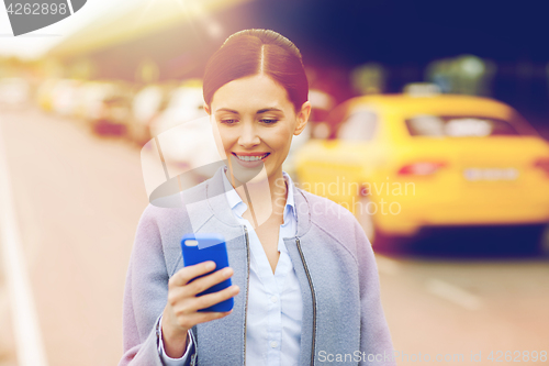 Image of smiling woman with smartphone over taxi in city