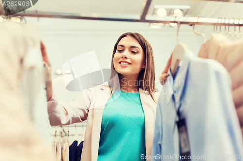 Image of happy young woman choosing clothes in mall