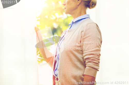 Image of lonely senior woman looking through window at home