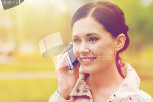 Image of smiling woman calling on smartphone in park