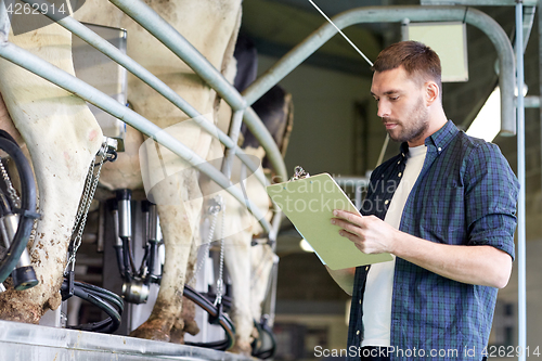 Image of man with clipboard and milking cows on dairy farm