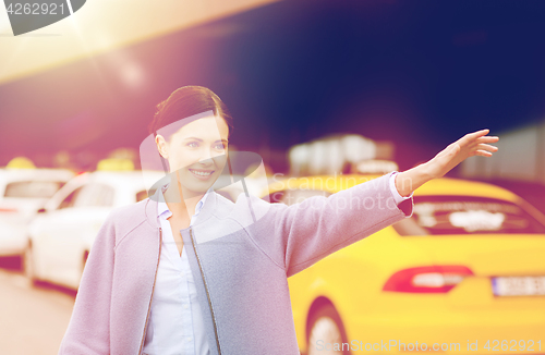 Image of smiling young woman waving hand and catching taxi