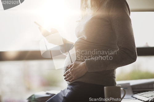 Image of pregnant businesswoman with smartphone at office