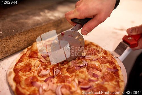 Image of cook hands cutting pizza to pieces at pizzeria