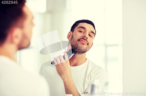 Image of man shaving beard with trimmer at bathroom