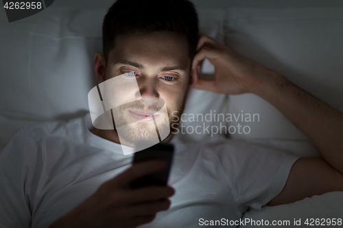 Image of young man with smartphone in bed at night