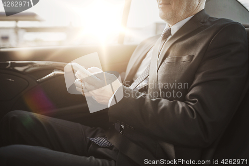 Image of senior businessman texting on smartphone in car