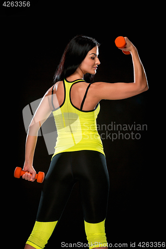 Image of The woman training against black studio with red dumbbells