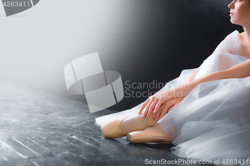 Image of Young ballerina, closeup on legs and shoes, sitting in pointe shooses