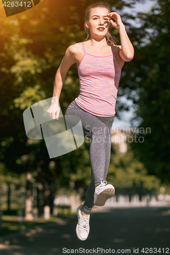 Image of Pretty sporty woman jogging at park in sunrise light