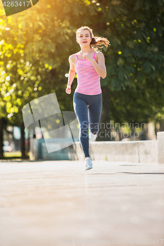 Image of Pretty sporty woman jogging at park in sunrise light