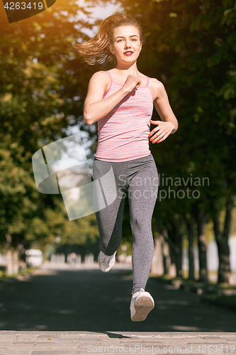 Image of Pretty sporty woman jogging at park in sunrise light