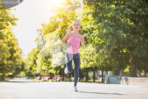 Image of Pretty sporty woman jogging at park in sunrise light