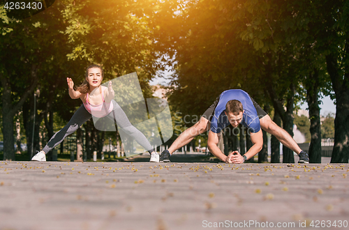 Image of Fit fitness woman and man doing stretching exercises outdoors at park