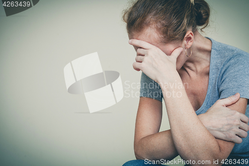 Image of one sad woman sitting near a wall